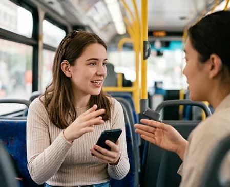 A young woman holding a phone and talking with a support worker on a public bus